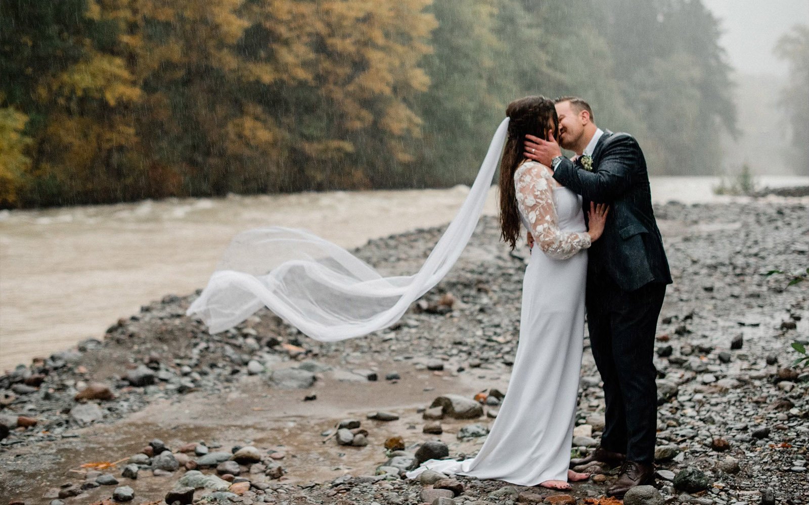 https://ruffledroseveils.com/wp-content/uploads/2023/04/Ruffled-Rose-Veils-Ottawa-Canadian-handmade-bridal-veils-bride-in-modern-lace-and-minimalist-dress-kissing-new-husband-in-the-rain-on-a-rocky-beach-with-veil-flowing-out-behind-her.jpg